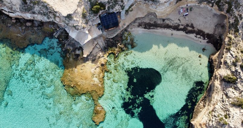 Luchtfoto van Cala Escondida (es Racó d'en Xic) bij Cala Comte op Ibiza, met een strookje zand, turquoise water en zeegras