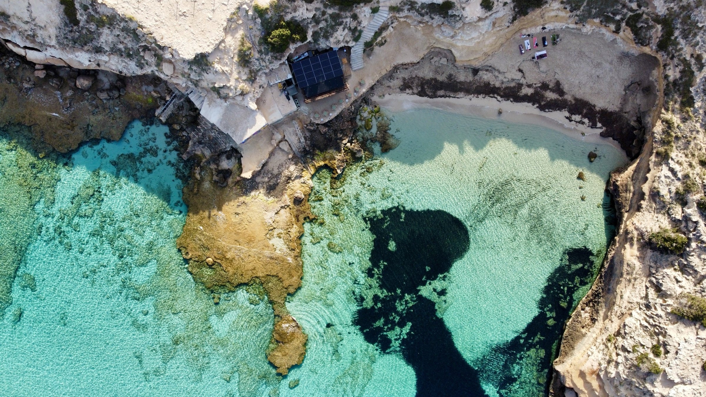 Luchtfoto van Cala Escondida (es Racó d'en Xic) bij Cala Comte op Ibiza, met een strookje zand, turquoise water en zeegras