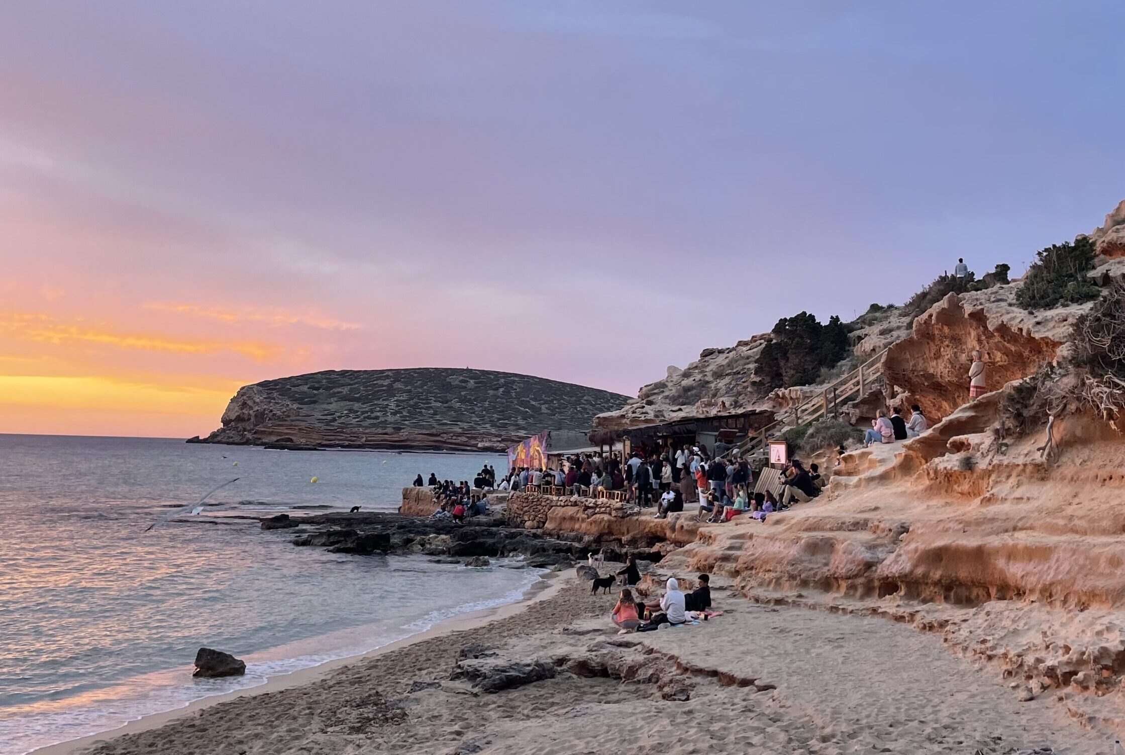 Het strandje van Cala Escondida bij zonsondergang, met de rotsen en het eilandje Illa des Bosc, Ibiza