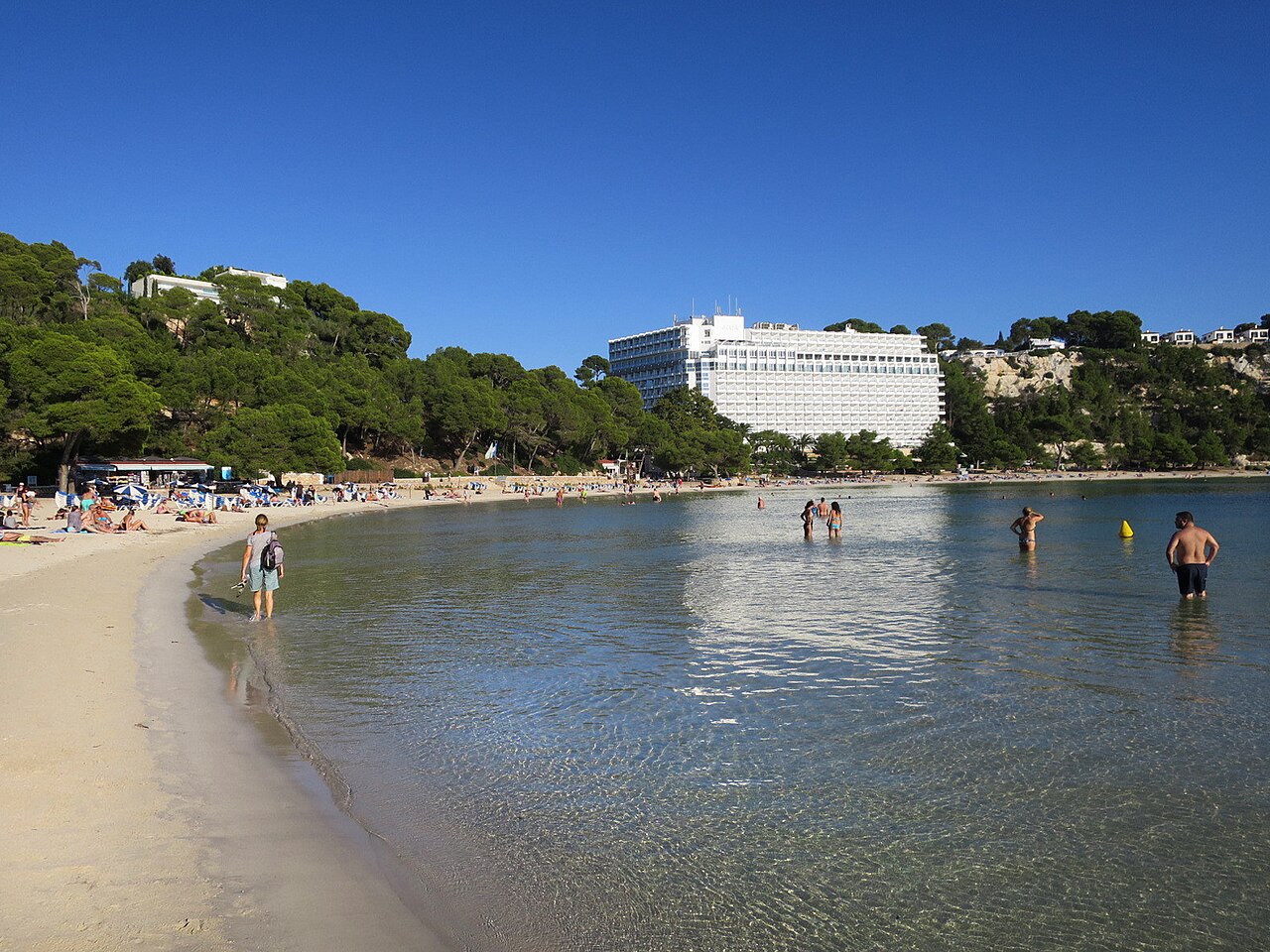 Cala Galdana Menorca: de baai, parkeren en lopen naar Macarella 2 Het ondiepe water aan het strand van Cala Galdana op Menorca, met een hotel tussen de pijnbomen