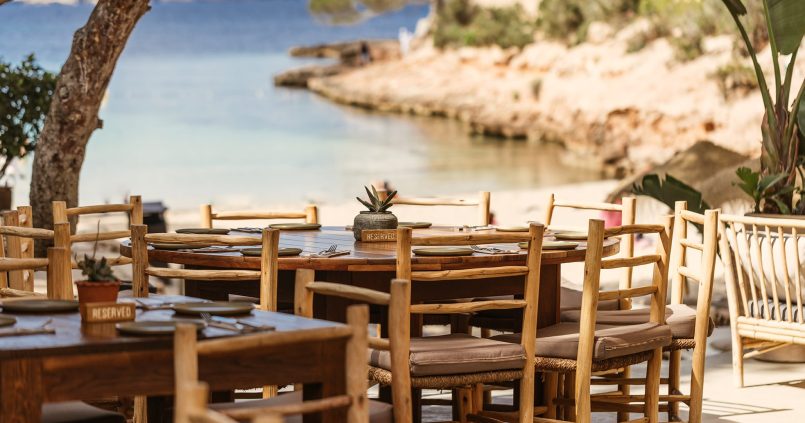 Het terras van het strandrestaurant van Cala Gracioneta met houten tafels en uitzicht op de kleine baai