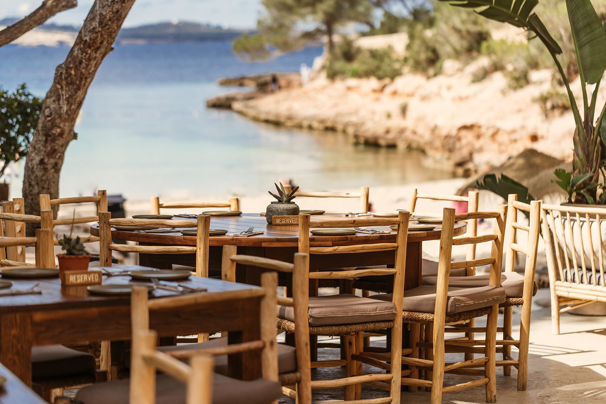 Cala Gracioneta Ibiza: verborgen mini-strand bij Sant Antoni 1 Het terras van het strandrestaurant van Cala Gracioneta met houten tafels en uitzicht op de kleine baai