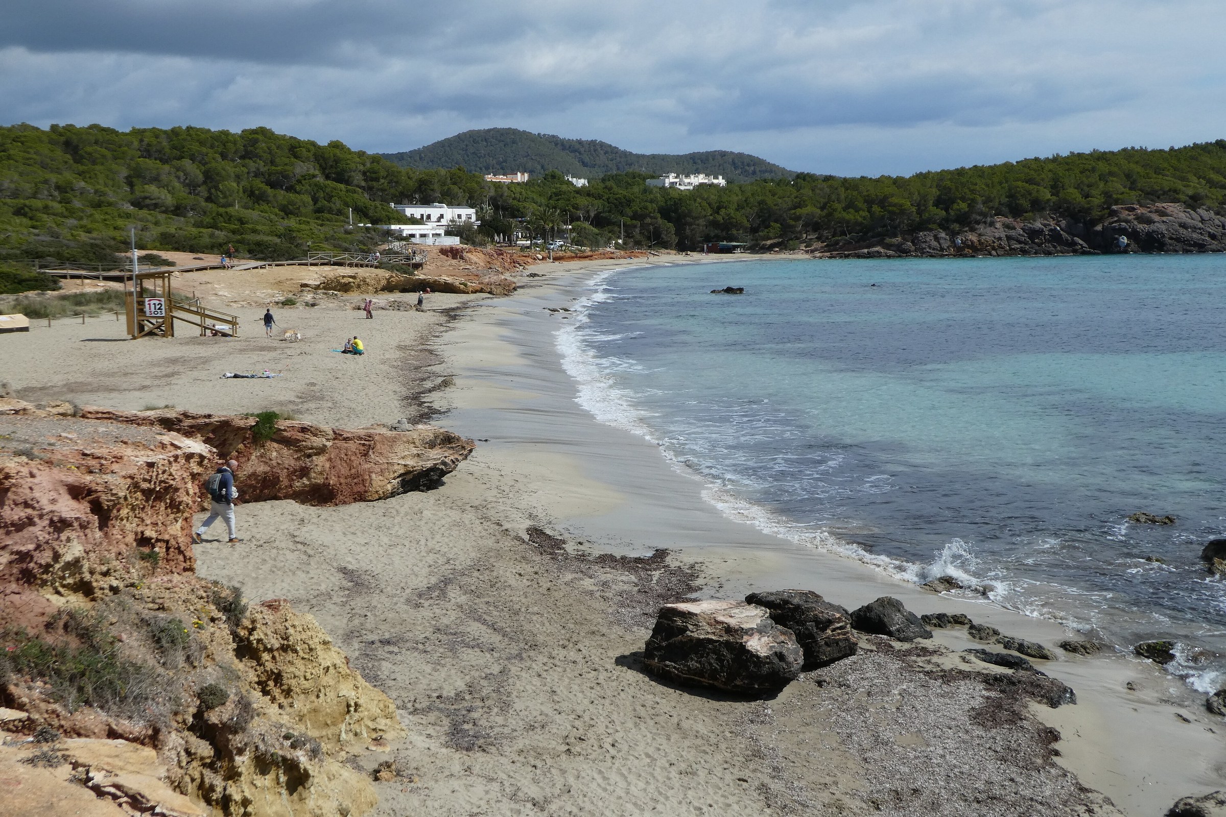 Het brede zandstrand van Cala Llenya op Ibiza met de reddingspost en roodbruine rotsen