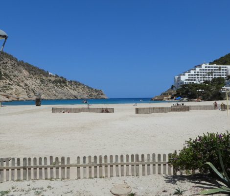 Het brede zandstrand van Cala Llonga met de smalle baai tussen twee beboste heuvels aan de oostkust van Ibiza