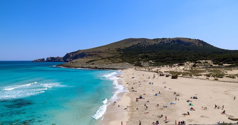 Het zandstrand van Cala Mesquida in het noordoosten van Mallorca met turquoise water en een beboste heuvel erachter