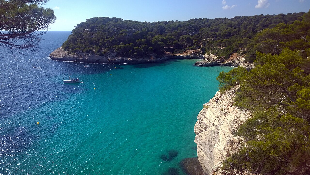 Het heldere turquoise water van Cala Mitjana op Menorca met witte kalksteenkliffen