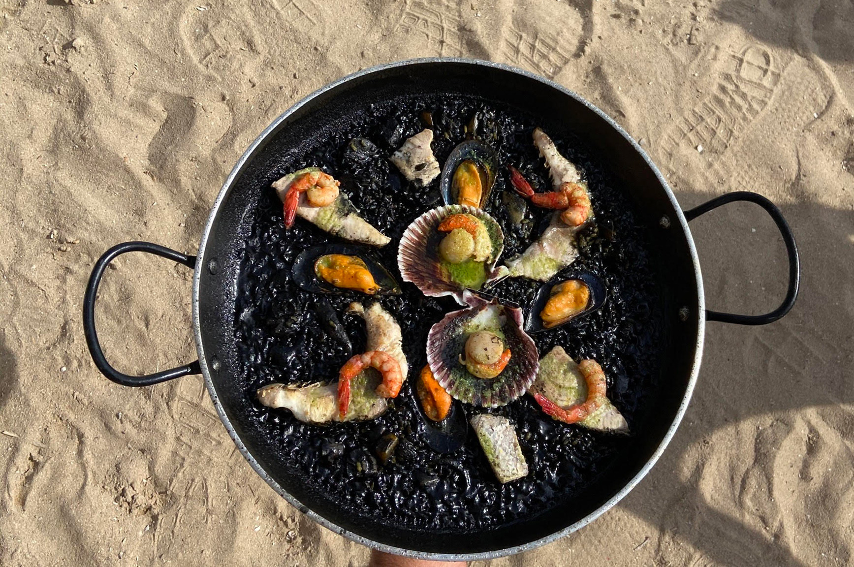 Pan zwarte rijst met schaaldieren op het zand van Cala Pada