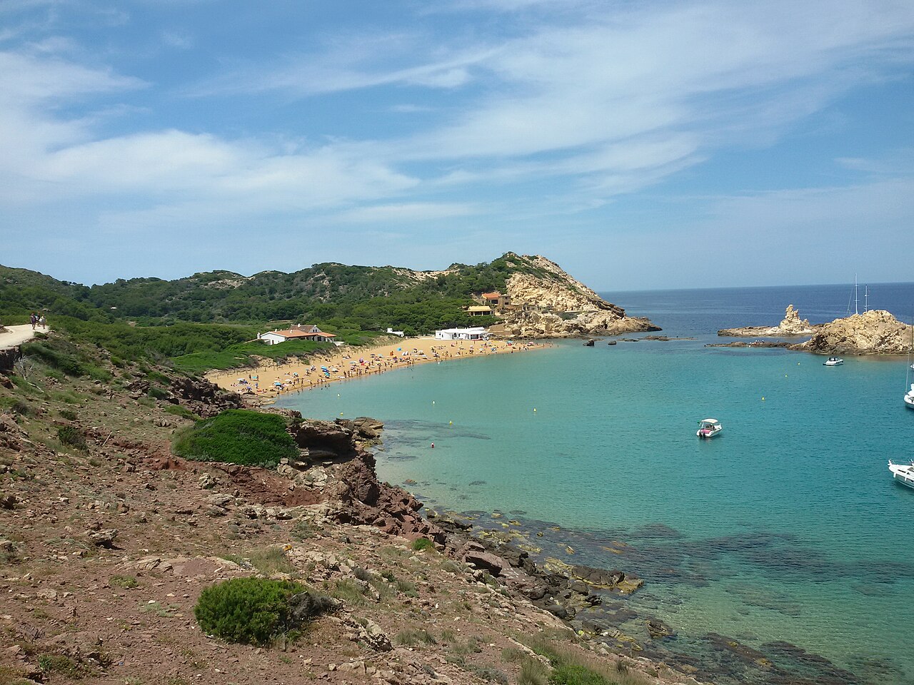 Overzicht van de baai van Cala Pregonda op Menorca met het roodgouden zand en de rotseilandjes voor de kust