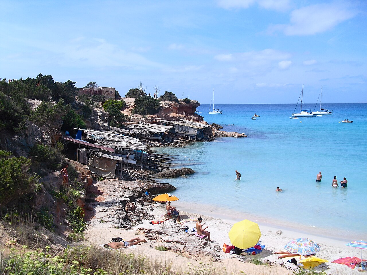 Houten bootgarages tegen de rode rotsen van Cala Saona op Formentera