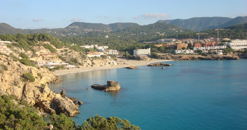 De baai van Cala Tarida aan de westkust van Ibiza met het eilandje in het turquoise water en de hotels op de heuvels