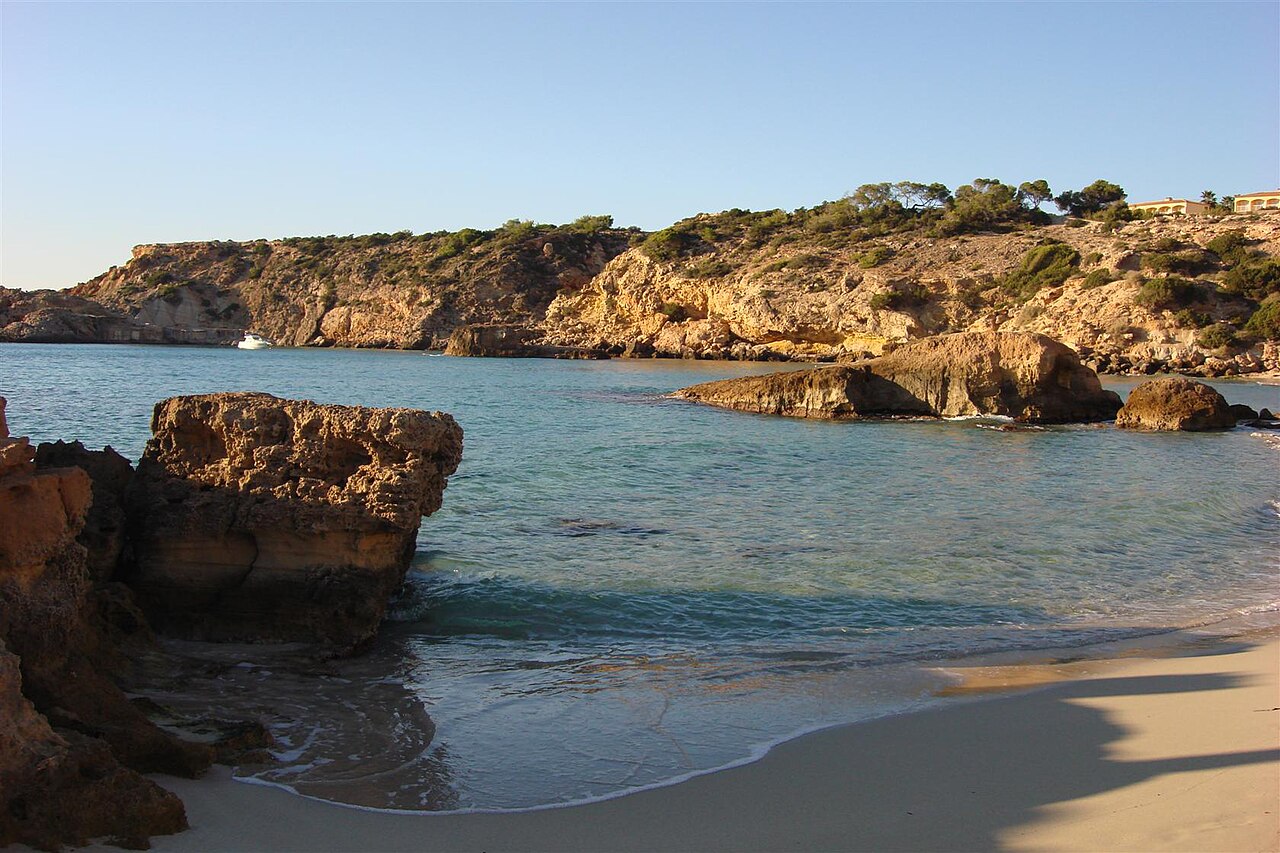 Cala Tarida Ibiza: het strand, de bussen A1 en P9 en parkeren 3 De waterlijn van Cala Tarida op Ibiza, met de rotsen aan de rand van de baai en het ondiepe heldere water