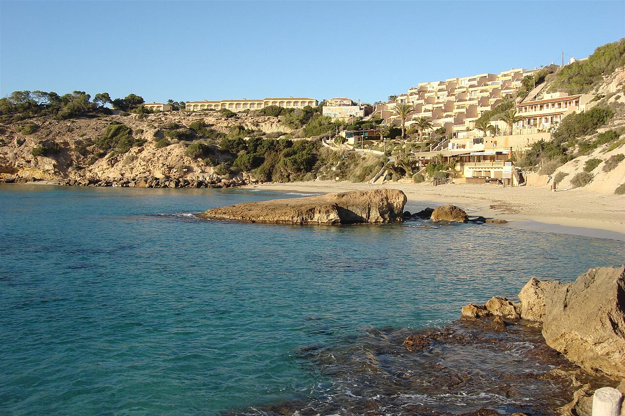 Cala Tarida Ibiza: het strand, de bussen A1 en P9 en parkeren 4 De baai van Cala Tarida op Ibiza vanaf het zand gezien, met de rots in het water en de hotels op de heuvel erachter
