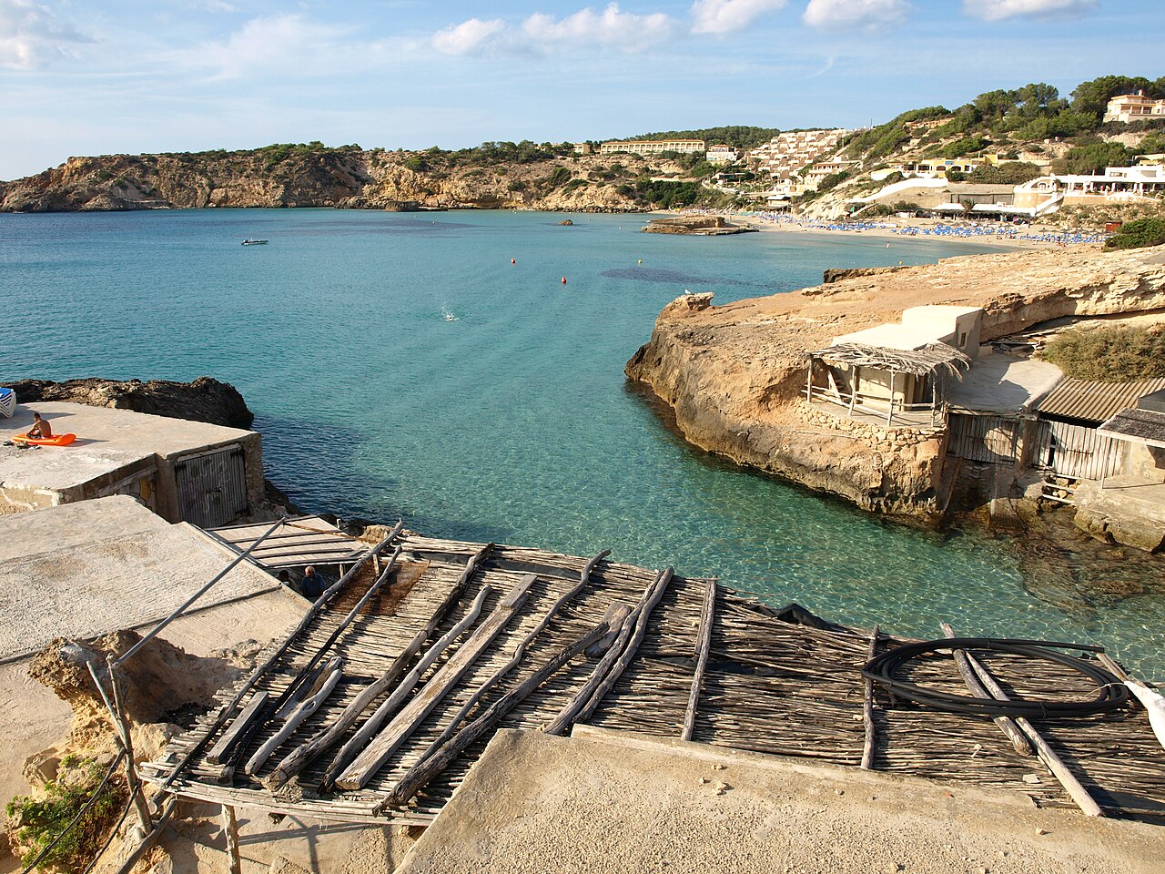 Cala Tarida Ibiza: het strand, de bussen A1 en P9 en parkeren 7 De houten vissershuisjes met hun helling aan de rotsige kant van Cala Tarida op Ibiza, met het strand aan de overkant van de baai
