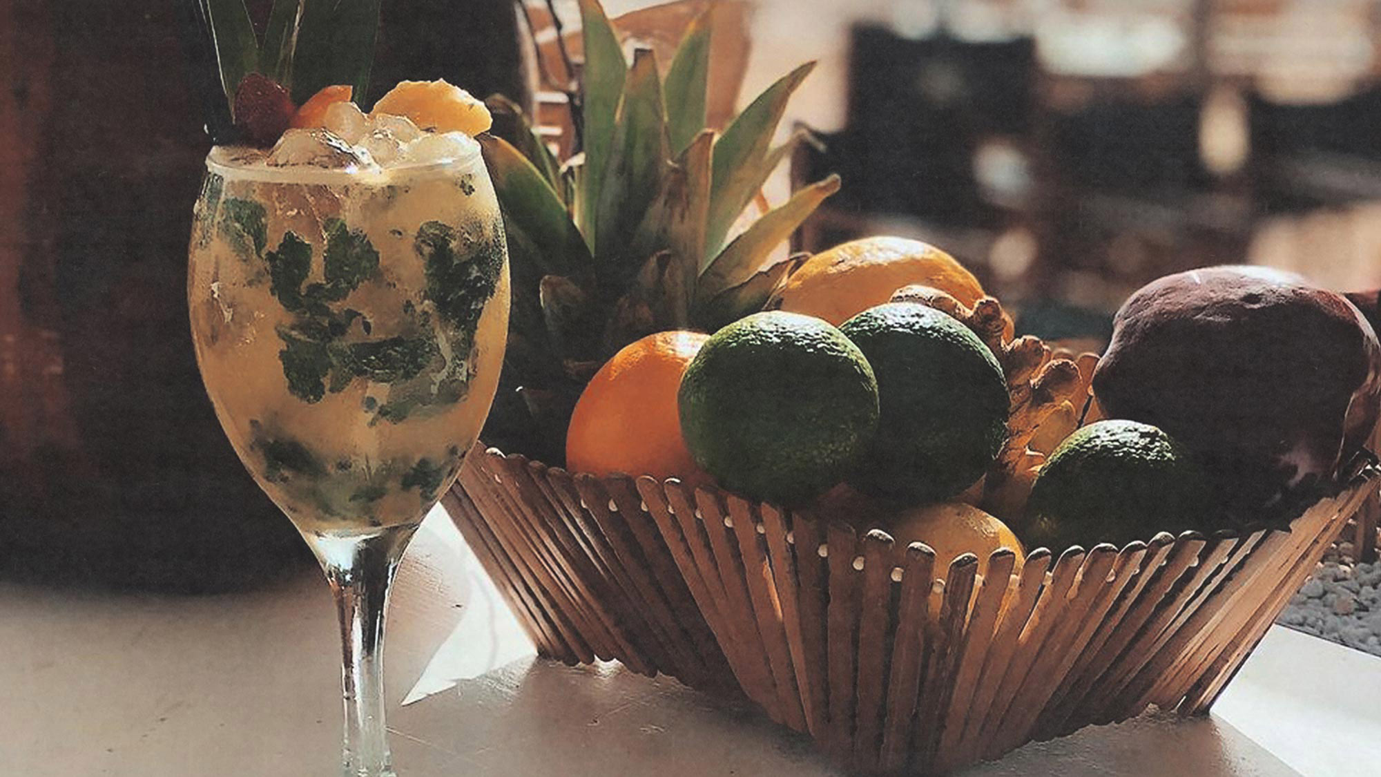Een cocktail en een mand met vers fruit op een tafel bij Can Carlitos
