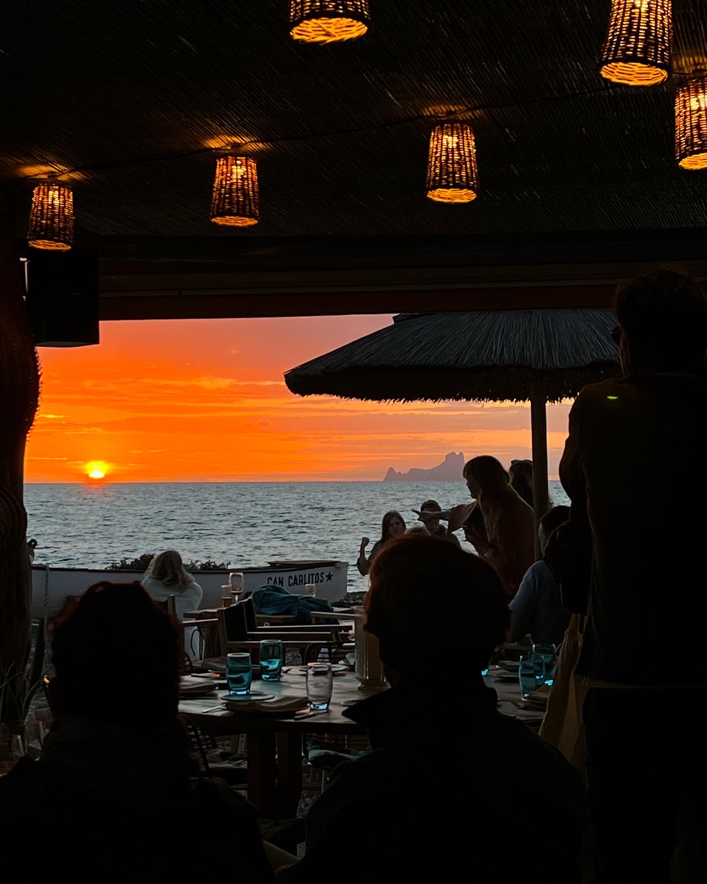 Het terras van Can Carlitos met lampen en zicht op de zee bij zonsondergang