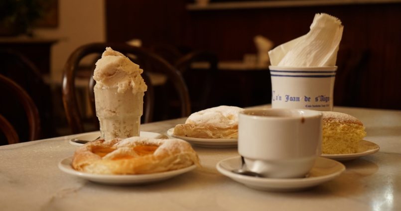 Marmeren tafeltje bij Ca'n Joan de s'Aigo in Palma met een glas ijs, ensaïmades, een quarto en een kop warme chocolade