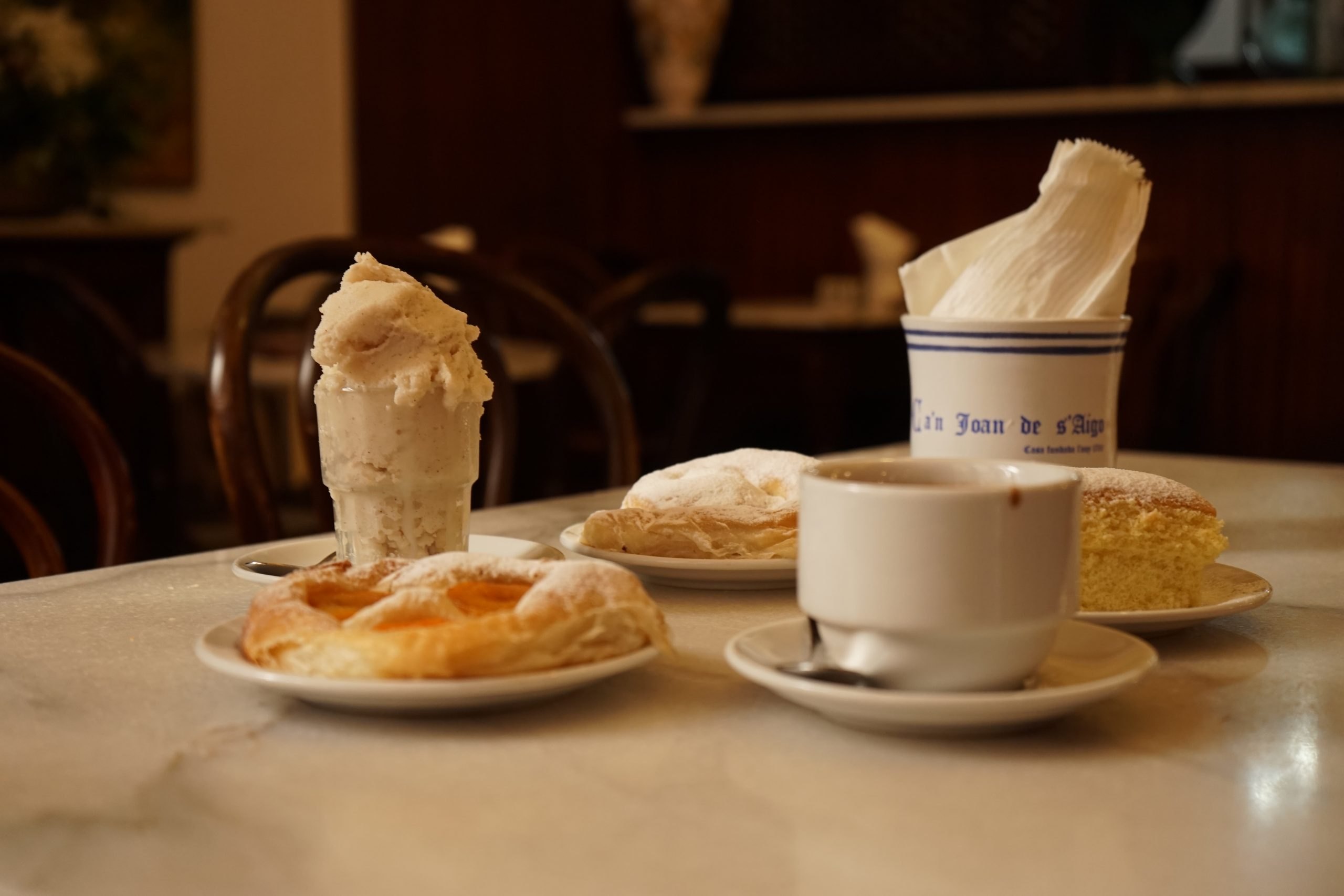 Marmeren tafeltje bij Ca'n Joan de s'Aigo in Palma met een glas ijs, ensaïmades, een quarto en een kop warme chocolade