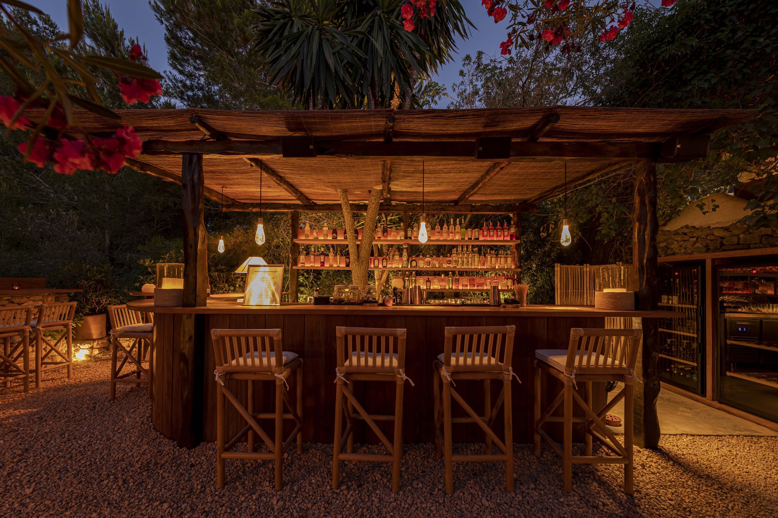 De cocktailbar van Casa Linda onder een houten overkapping in de tuin, met barkrukken en een wand vol flessen