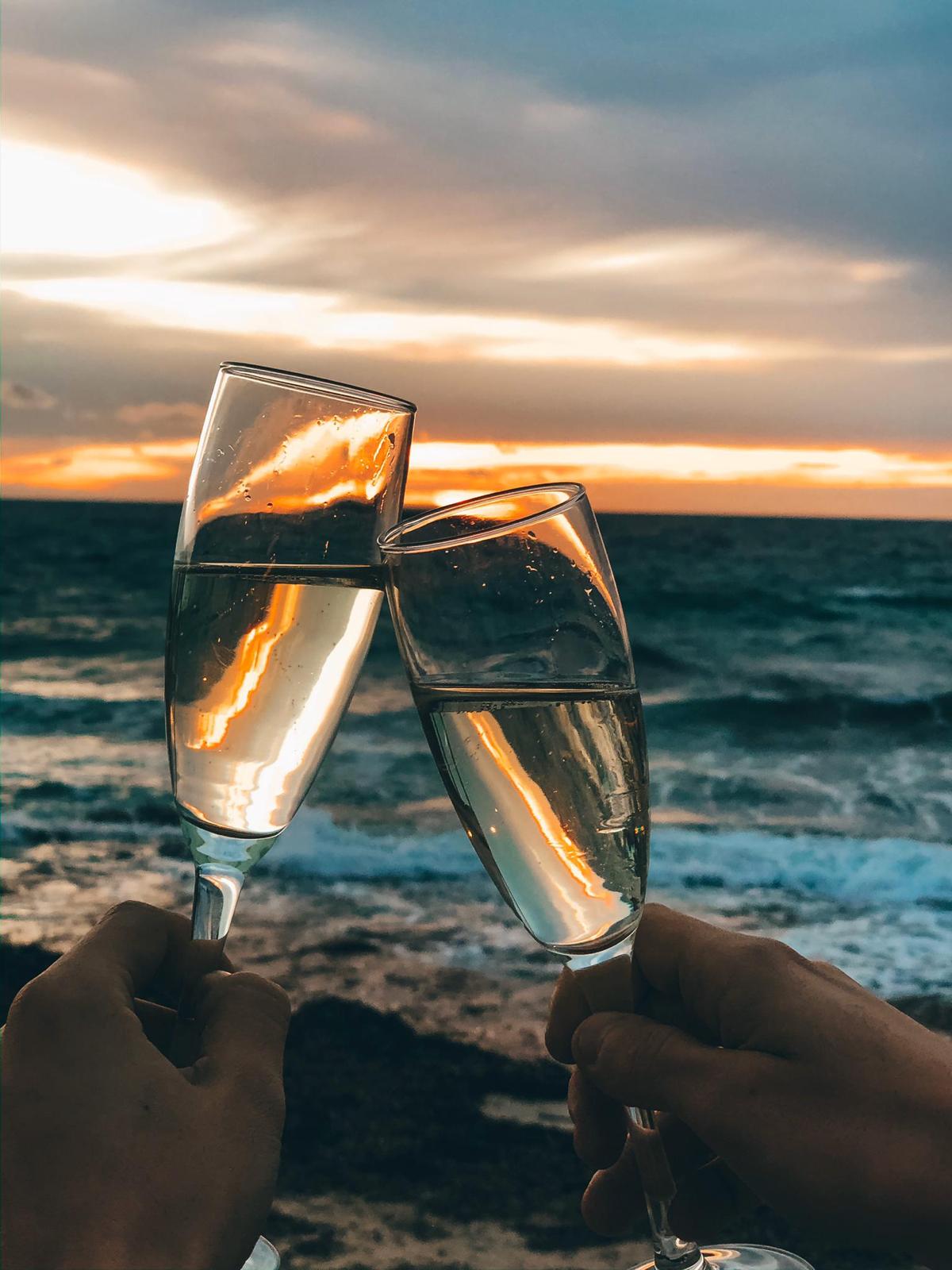Twee glazen cava geproost tegen de ondergaande zon boven de zee bij Cassai Beach House