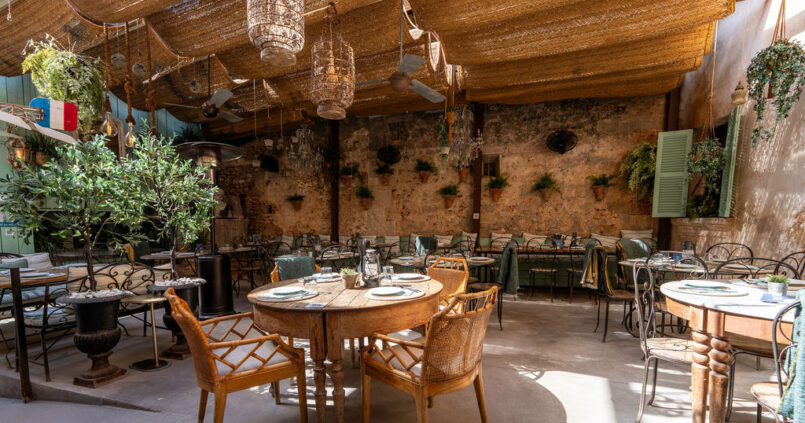 De overdekte patio met pergola, tafels en planten van Cassai Gran Café in Ses Salines