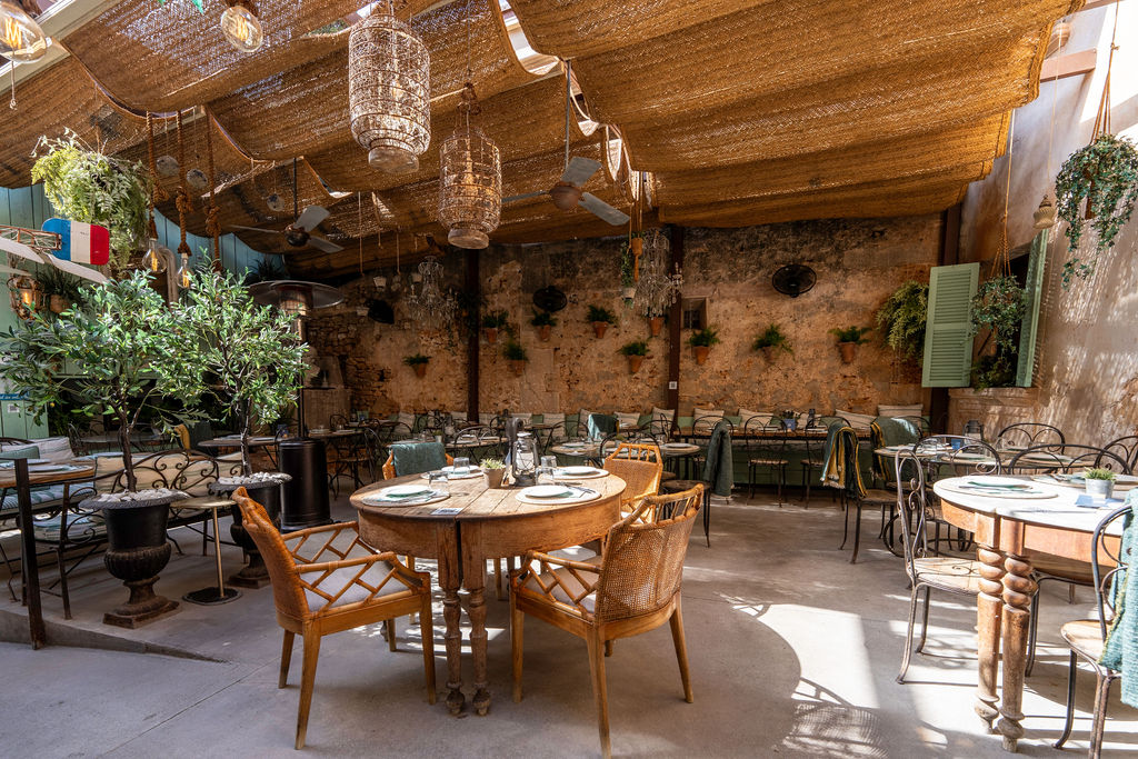 Cassai Gran Café Ses Salines: mediterraan eten in een oud dorpspand 1 De overdekte patio met pergola, tafels en planten van Cassai Gran Café in Ses Salines