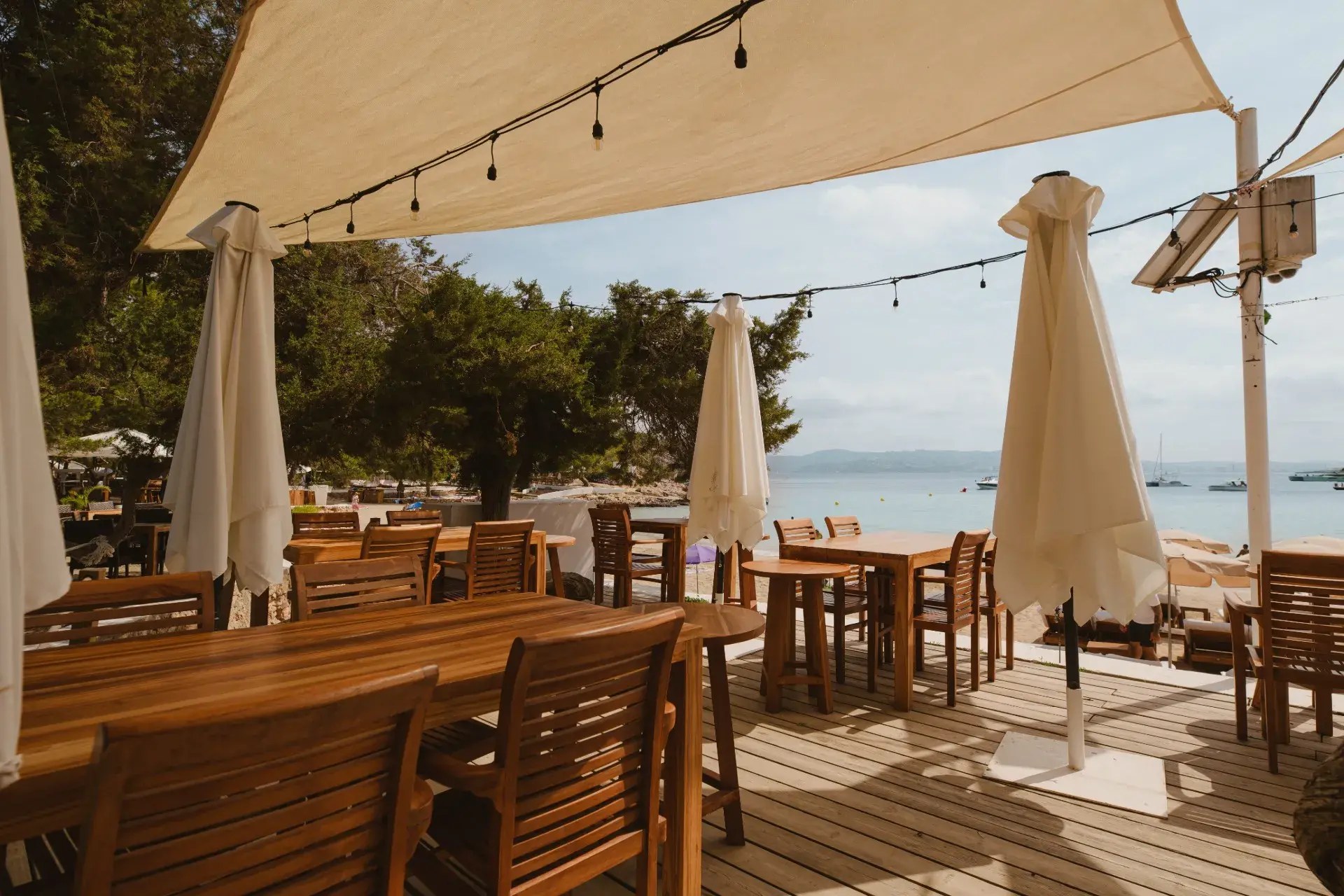 Cala Bassa Beach Club (CBbC) Ibiza: ligbedden, restaurants en prijzen 2026 4 Houten restaurantterras van Cala Bassa Beach Club onder een zeil met lichtsnoeren en uitzicht op zee