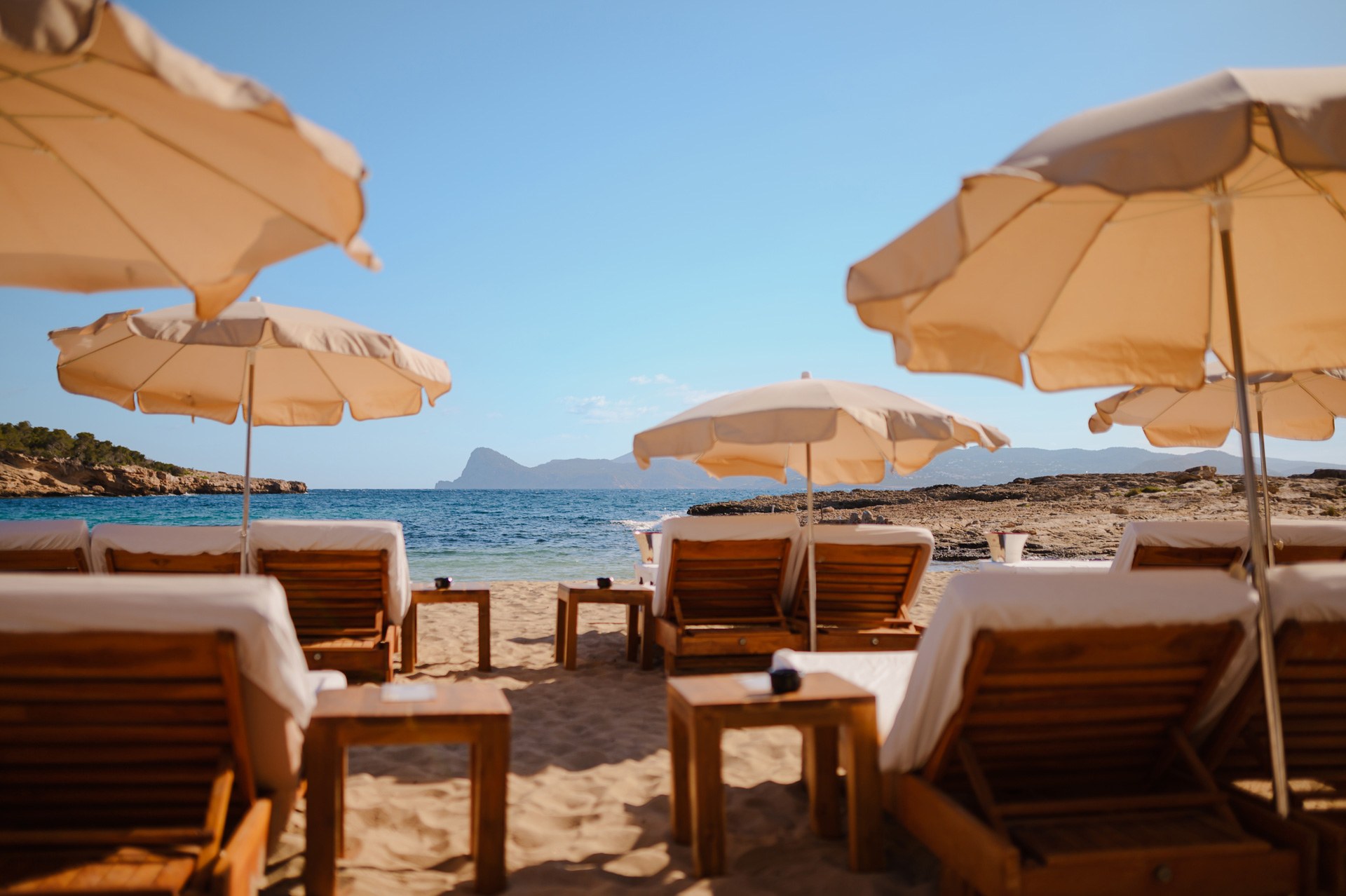 Cala Bassa Beach Club (CBbC) Ibiza: ligbedden, restaurants en prijzen 2026 2 Ligbedden met witte kussens en crèmekleurige parasols op de eerste rij van Cala Bassa Beach Club, met zicht op zee