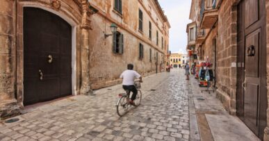 Parkeren op Menorca: camera's in Maó, blauwe zones en de stranden die dichtgaan 17 Smalle geplaveide straat in het centrum van Ciutadella op Menorca met een fietser