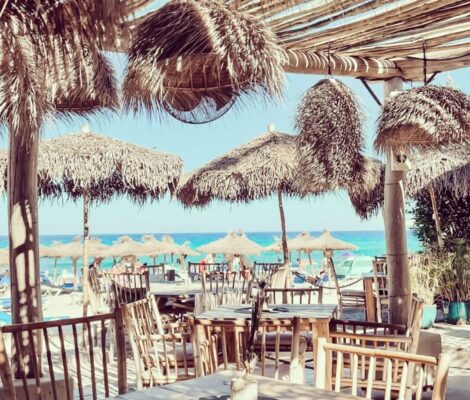 Het terras van Cucum Beach House met rieten parasols en uitzicht op de zee bij Playa Son Moll