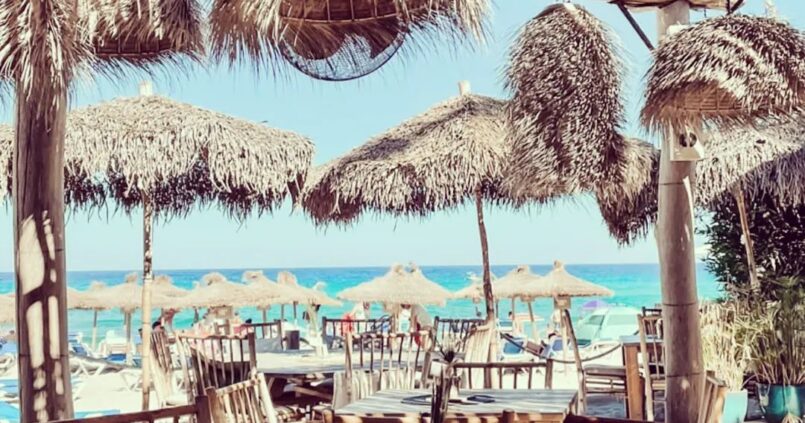 Het terras van Cucum Beach House met rieten parasols en uitzicht op de zee bij Playa Son Moll