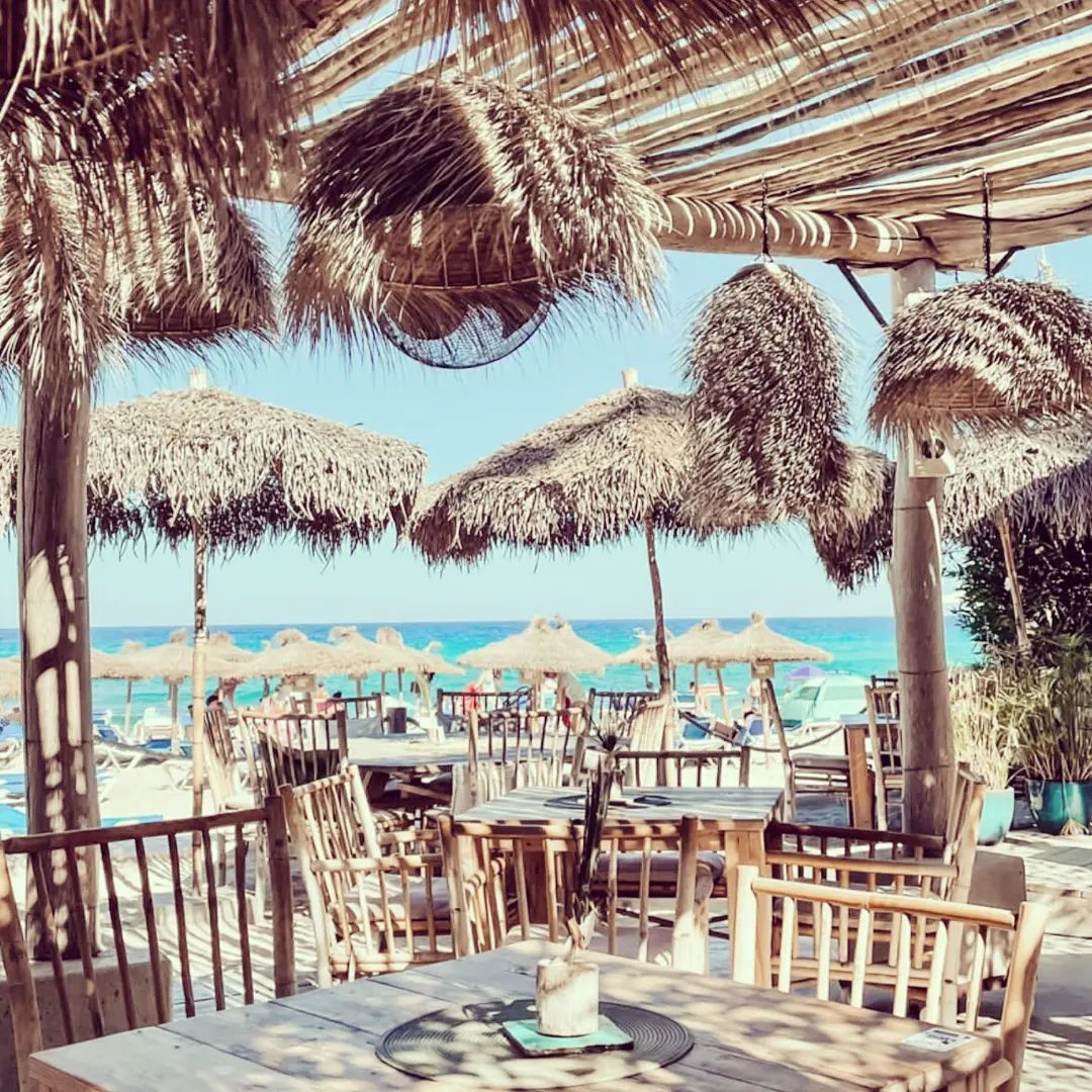 Het terras van Cucum Beach House met rieten parasols en uitzicht op de zee bij Playa Son Moll