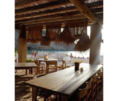 Lange houten eettafels onder een rieten dak met zeezicht bij El Silencio Ibiza