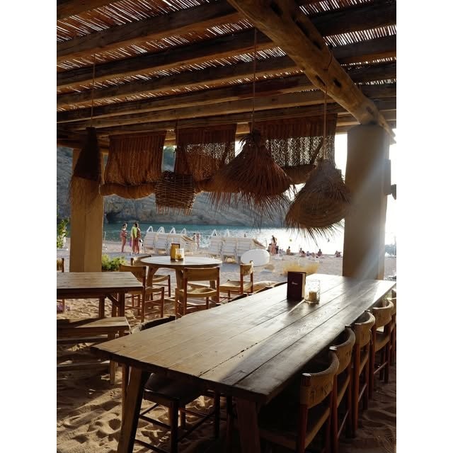 Lange houten eettafels onder een rieten dak met zeezicht bij El Silencio Ibiza