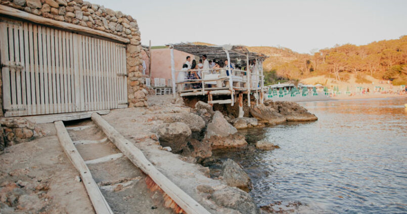 Het terras van Elements Ibiza op palen boven het water bij Cala Benirràs, naast de oude stenen boothuizen
