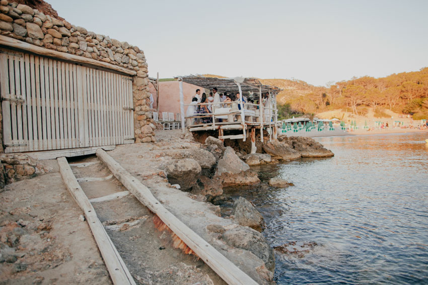Het terras van Elements Ibiza op palen boven het water bij Cala Benirràs, naast de oude stenen boothuizen