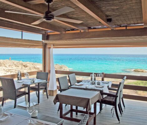 Het overdekte terras met gedekte tafels van Restaurante Es Caló boven de turquoise zee op Formentera