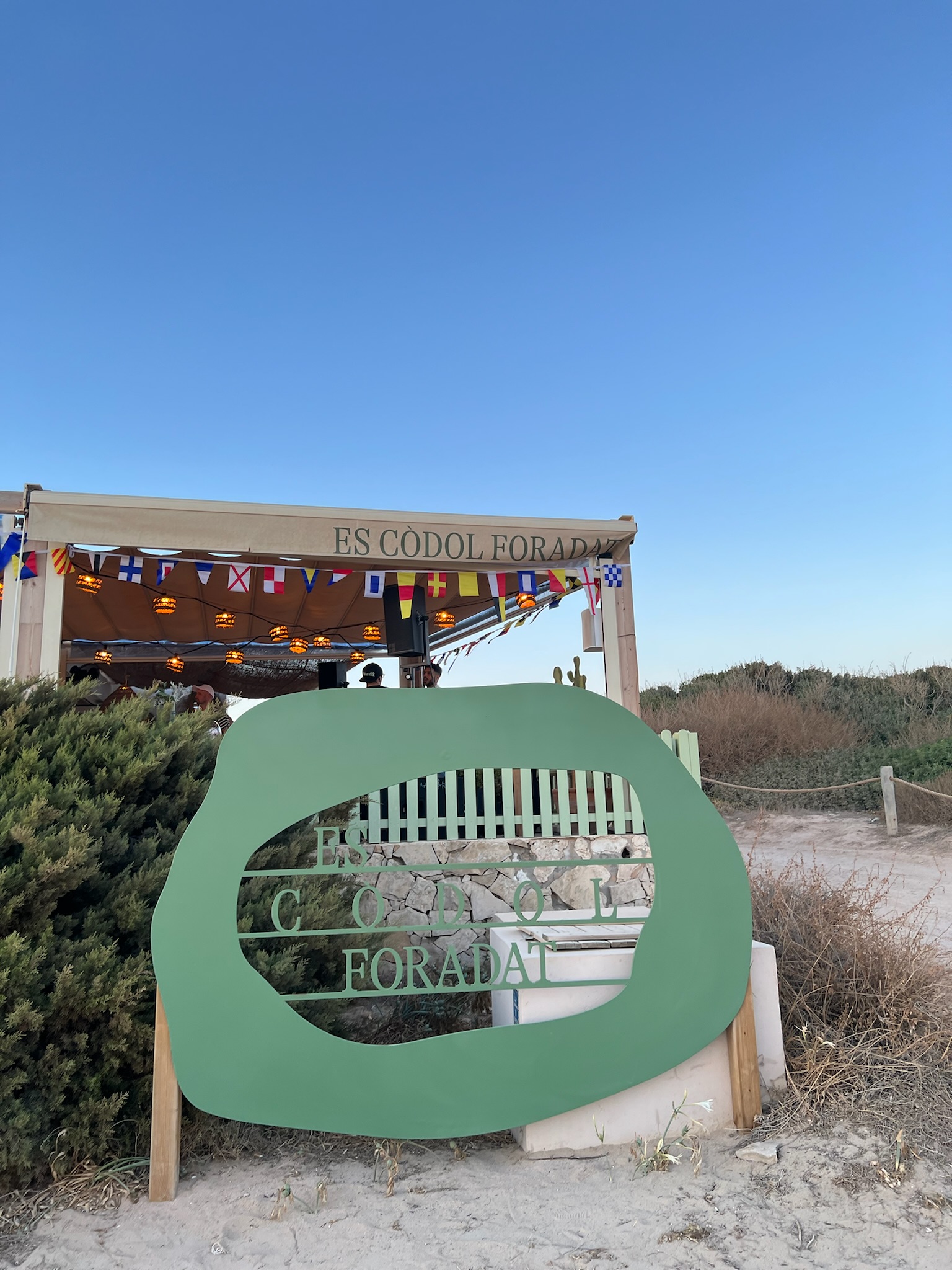 Het groene naambord van Es Còdol Foradat bij de ingang van de chiringuito in de avond