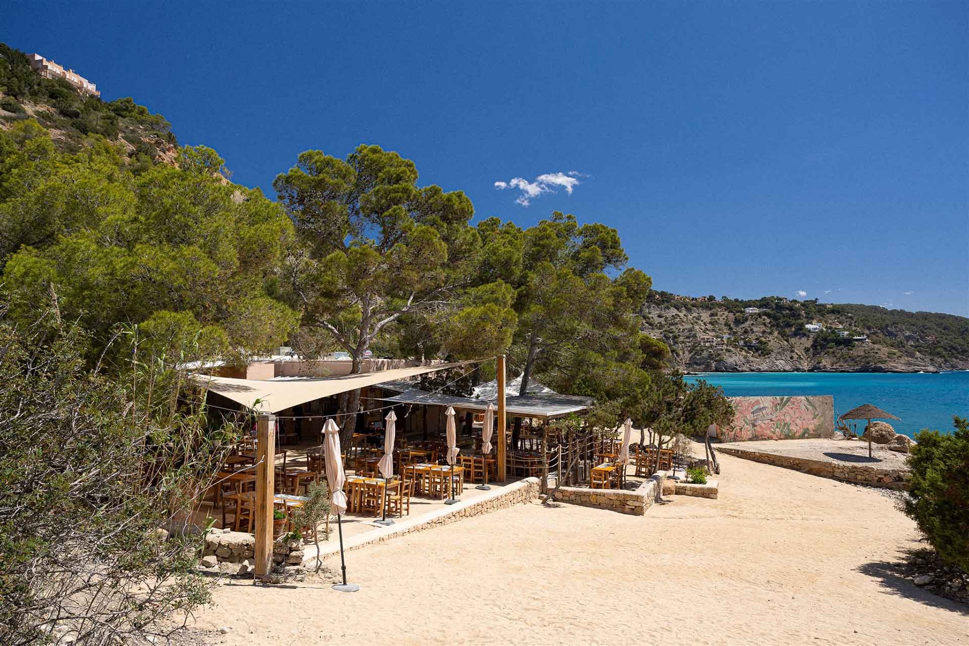 Het restaurant van Ses Boques tussen de pijnbomen aan de baai onder Es Cubells, met turquoise water en kliffen