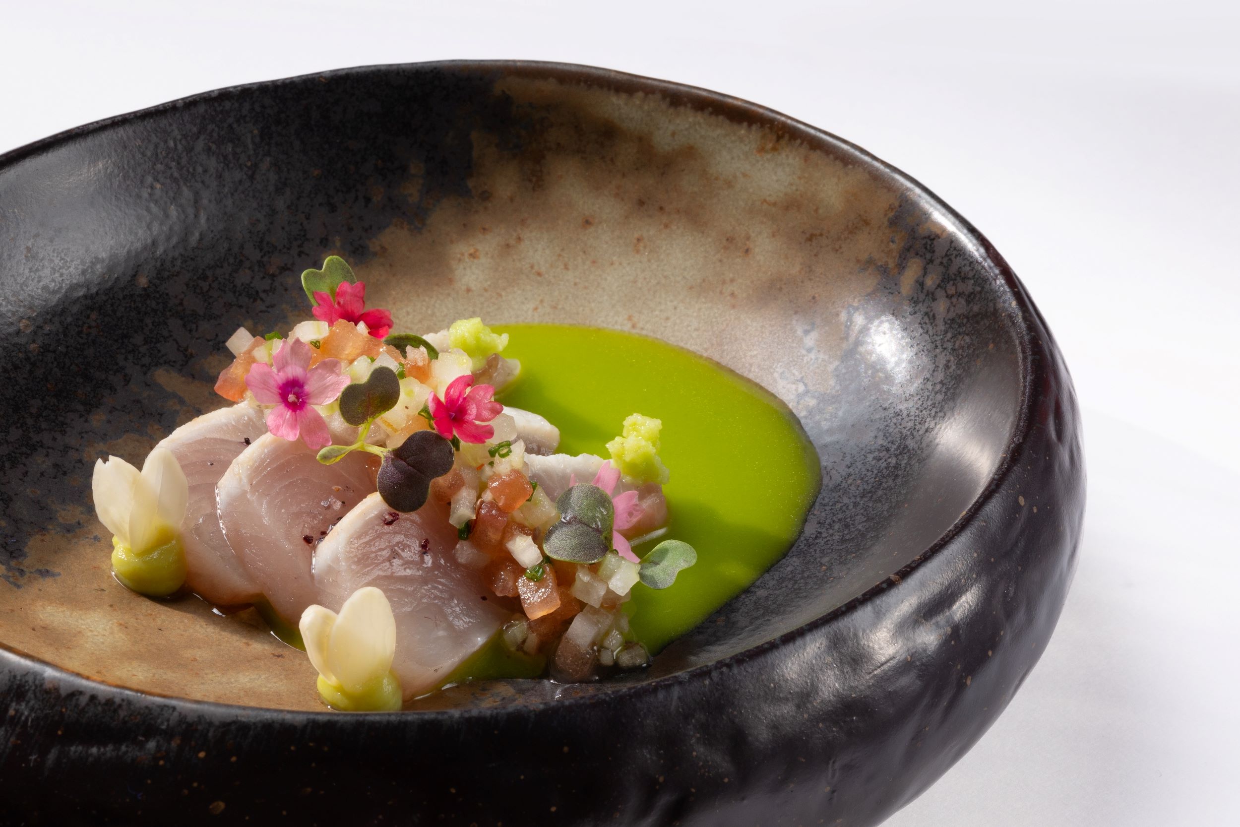 Es Fum bij Palmanova: sterrenkeuken op een terras aan zee 2 De hamachi van Es Fum op Mallorca, met gele staartvis, groene saus en eetbare bloemen in een donkere kom