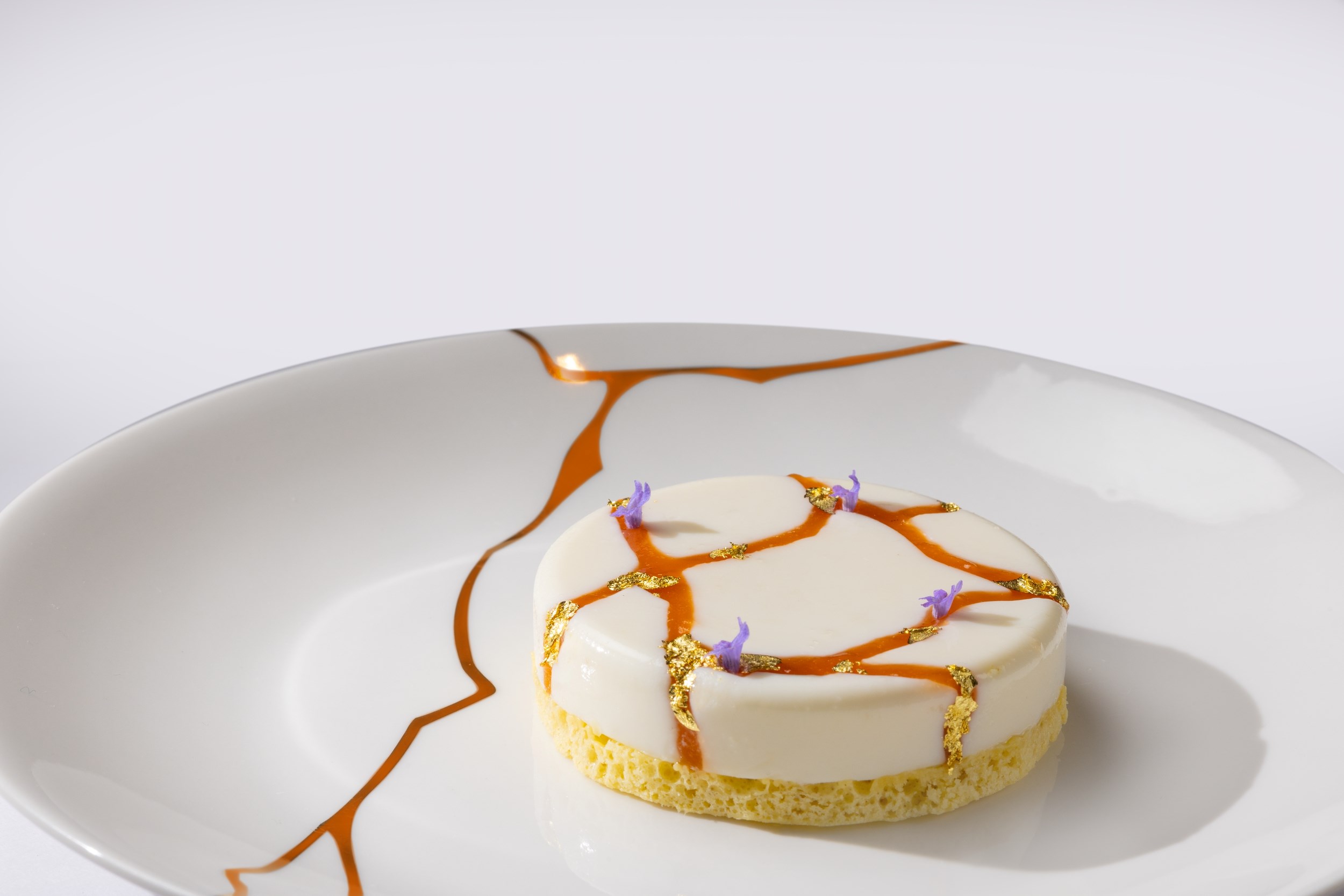 Es Fum bij Palmanova: sterrenkeuken op een terras aan zee 5 Dessert met lavendelkefir en karamellijnen op een wit bord bij Es Fum op Mallorca