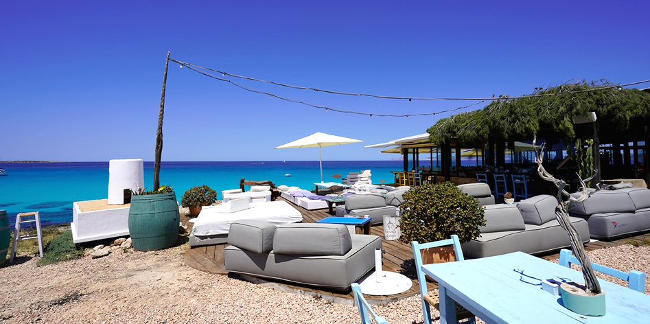 De chill-out met loungebedden en parasols aan het water van Ses Illetes bij Es Molí de Sal
