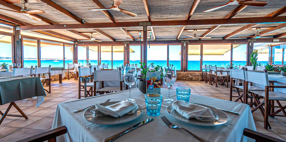 De eetzaal van Es Molí de Sal met gedekte tafels en panoramisch uitzicht over het turquoise water van Ses Illetes