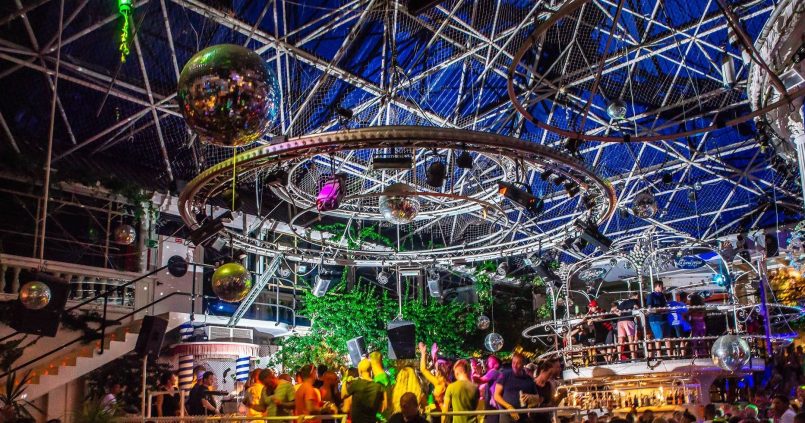 Het stalen frame van de glazen piramide boven de dansvloer van Es Paradís met discobollen en groen