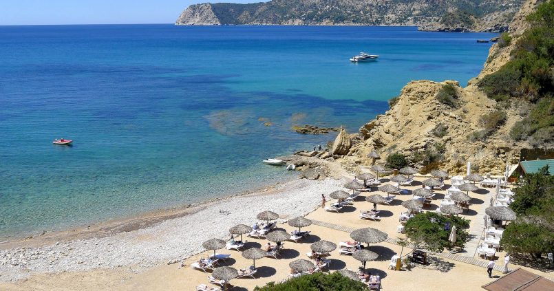 De kiezelbaai van Es Torrent op Ibiza van bovenaf, met strandparasols, helder water en de kliffen van Porroig