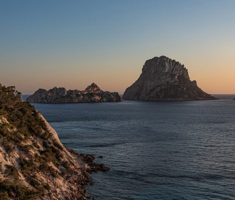 De rotseilanden Es Vedrà en Es Vedranell voor de zuidwestkust van Ibiza bij zonsondergang, gezien vanaf de beboste klif