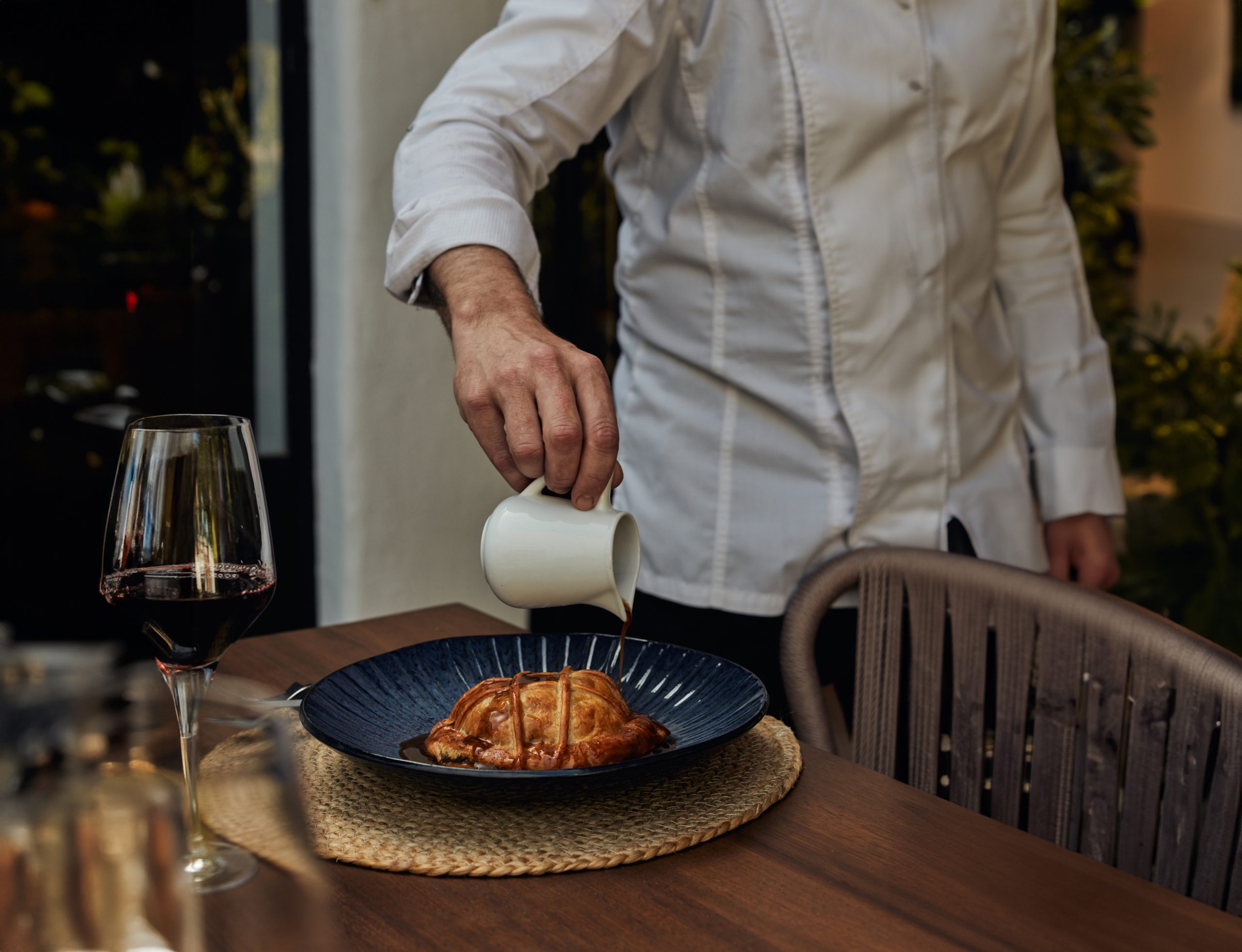 Finca La Plaza Ibiza: fine dining op de binnenplaats van Santa Gertrudis 2 Aan tafel wordt een gerecht afgemaakt bij Finca La Plaza, met een glas wijn ernaast