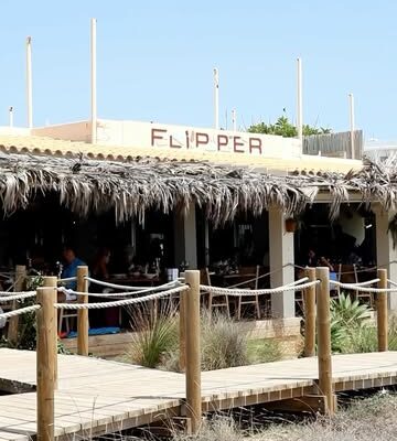 De strandingang van Flipper aan Platja des Arenals met het naambord en rieten daken