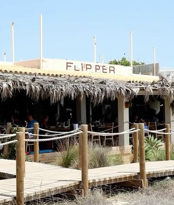 De strandingang van Flipper aan Platja des Arenals met het naambord en rieten daken