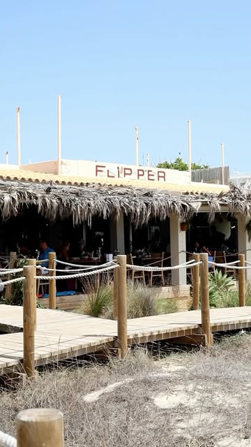 De strandingang van Flipper aan Platja des Arenals met het naambord en rieten daken