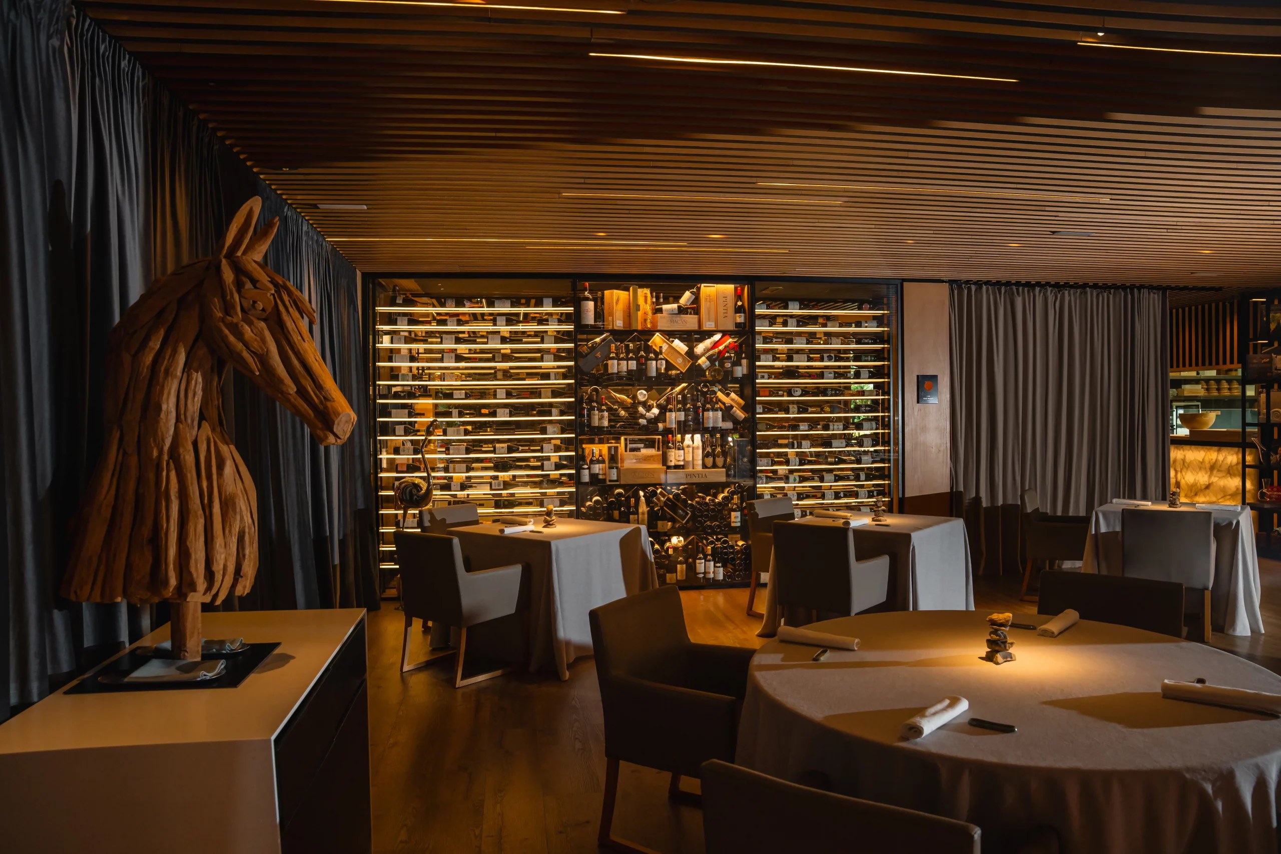 De zaal van Fusion19 op Mallorca met een houten paardensculptuur voor de verlichte wijnkelder